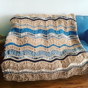 May include: A chunky knit throw blanket with a wavy pattern in shades of beige, blue, gray, and black.