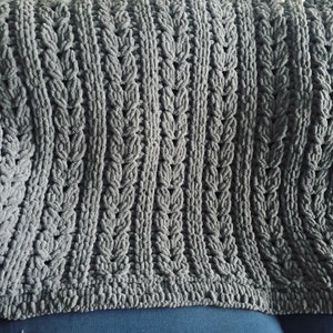 May include: A gray knitted throw blanket with a cable knit pattern. The blanket is soft and fluffy, and it would be perfect for cuddling up on the couch.