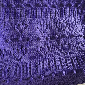 May include: A purple knitted blanket with a textured pattern and pom-poms along the edges.