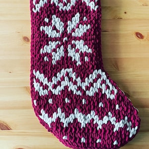May include: A red and white knitted stocking with a snowflake pattern. The stocking is made of a soft, fluffy yarn.