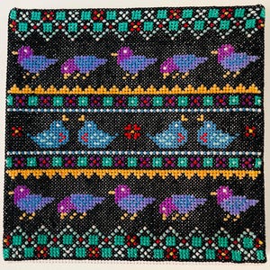 May include: A square, black, cross-stitched textile with a repeating pattern of birds and geometric designs. The birds are blue and purple, with yellow beaks and feet. The borders and bands feature teal, red, and gold accents, creating a vibrant, folk-art style.