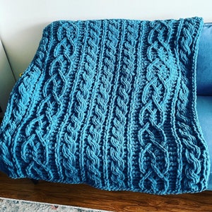May include: A teal blue knitted throw blanket with a cable knit pattern.