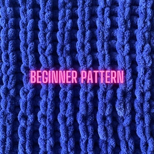 May include: A close-up of a blue knitted blanket with a textured, puffy surface. The text "BEGINNER PATTERN" is written in pink across the middle of the blanket.