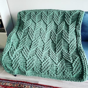 May include: A green crocheted throw blanket with a chevron pattern. The blanket is made with a thick yarn and has a soft, fuzzy texture.