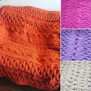 Op de afbeelding: Vier gehaakte dekens in verschillende kleuren: oranje, roze, paars en crème. De dekens hebben een textuurpatroon met verhoogde bobbels en een geweven ontwerp.