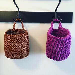 May include: Two hanging baskets, one brown and woven, the other purple and crocheted.