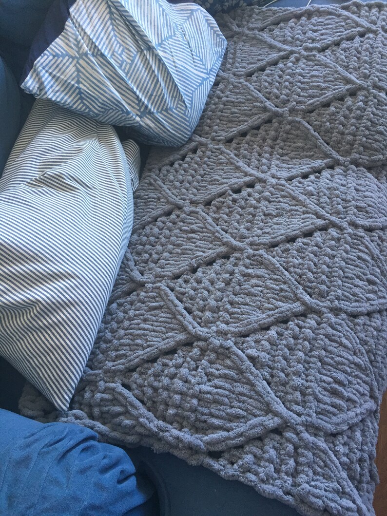 May include: A gray, textured throw blanket with a diamond pattern. The blanket is made of soft, fluffy yarn and has a cozy feel.
