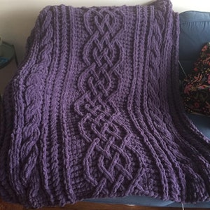 Peut inclure: Une couverture en tricot de couleur violette avec un motif en tricot torsadé. La couverture est douce et moelleuse et serait parfaite pour se blottir sur le canapé.