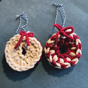 May include: Two crocheted wreaths, one white and one red and white, with red bows. The wreaths are hanging from white string with blue stripes.