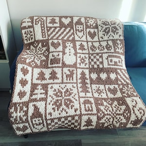 Könnte beinhalten: Eine braune und weiße gestrickte Wolldecke mit geometrischem Muster. Die Decke ist aus dickem Garn gefertigt und hat eine weiche, kuschelige Textur.