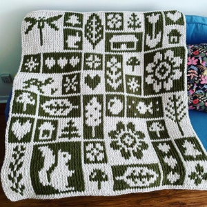 May include: A knitted blanket with a repeating pattern of green and white squares. Each square features a different nature-themed design, including trees, hearts, and flowers. The blanket is draped over a blue couch.