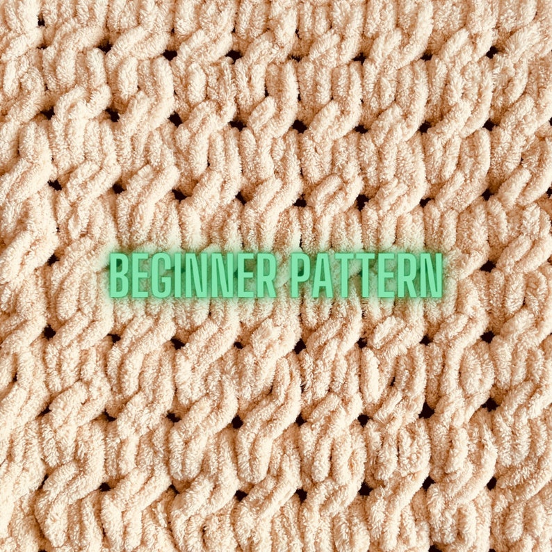 May include: A close-up of a beige knitted fabric with a woven pattern. The fabric has a soft, fluffy texture and is made with a chunky yarn. The text "BEGINNER PATTERN" is printed on the fabric.