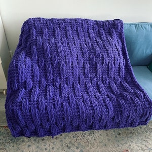 May include: A purple knitted throw blanket with a woven pattern. The blanket is soft and fluffy, and it would be perfect for snuggling up on the sofa.