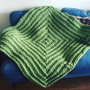 May include: A green knitted throw blanket with a square pattern. The blanket is draped over a blue sofa.