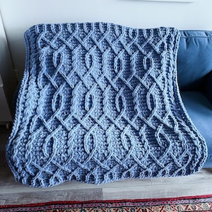 May include: A blue knitted throw blanket with a diamond pattern. The blanket is made with a chunky yarn and has a soft, cosy texture.