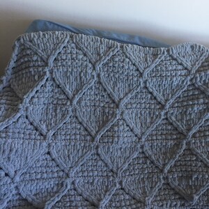 May include: A gray knitted throw blanket with a diamond pattern. The blanket is made of a soft, fluffy material and has a textured surface.