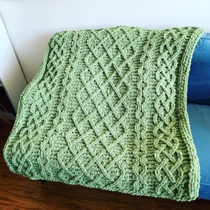 May include: A green crocheted throw blanket with a diamond pattern. The blanket is made with a thick yarn and has a soft, fuzzy texture.