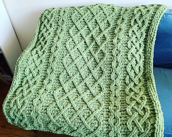 Pode incluir: Uma manta de crochê verde com um padrão de diamantes. A manta é feita com um fio grosso e tem uma textura macia e felpuda.
