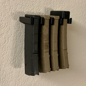 May include: A wall-mounted magazine holder with four black and tan magazines. The holder is made of black plastic and has a simple design.