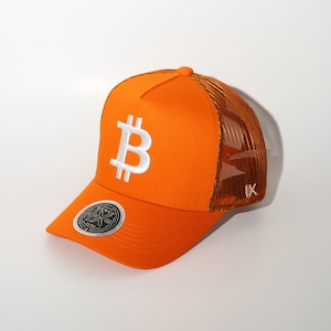 May include: Orange trucker hat featuring a white Bitcoin symbol on the front. The hat has a mesh back and a curved brim. A small logo is visible on the side and a circular emblem on the brim.