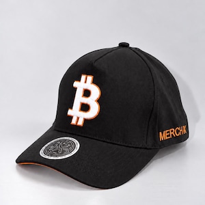 May include: A black baseball cap featuring a white Bitcoin symbol with an orange outline embroidered on the front. The side of the cap displays the text MERCHK in orange embroidery, and a circular sticker is attached to the brim.