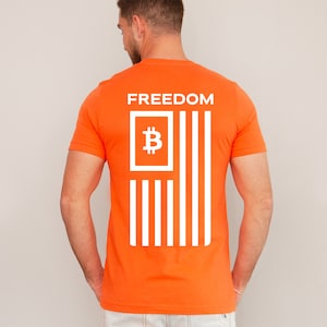 May include: Orange t-shirt with a white Bitcoin symbol inside a square and white stripes, resembling an American flag. The text "FREEDOM" is printed above the symbol.