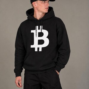 May include: A black hooded sweatshirt featuring a large white Bitcoin symbol printed on the chest, paired with a matching black baseball cap that displays a white Bitcoin logo on the front and the Roman numeral IX on the side.