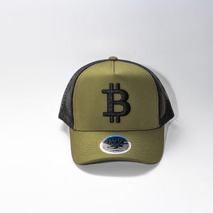 May include: Olive green trucker hat with a black mesh back and a black Bitcoin symbol embroidered on the front. The hat has a curved brim and a small button on top. A circular sticker is on the brim.