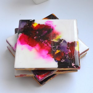 May include: Set of four square ceramic coasters with abstract art in shades of pink, yellow, purple, and black.