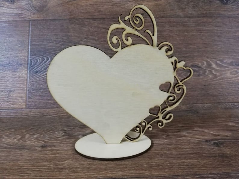May include: A wooden heart-shaped sign with a decorative scrollwork design. The sign is blank and can be used for a variety of purposes.