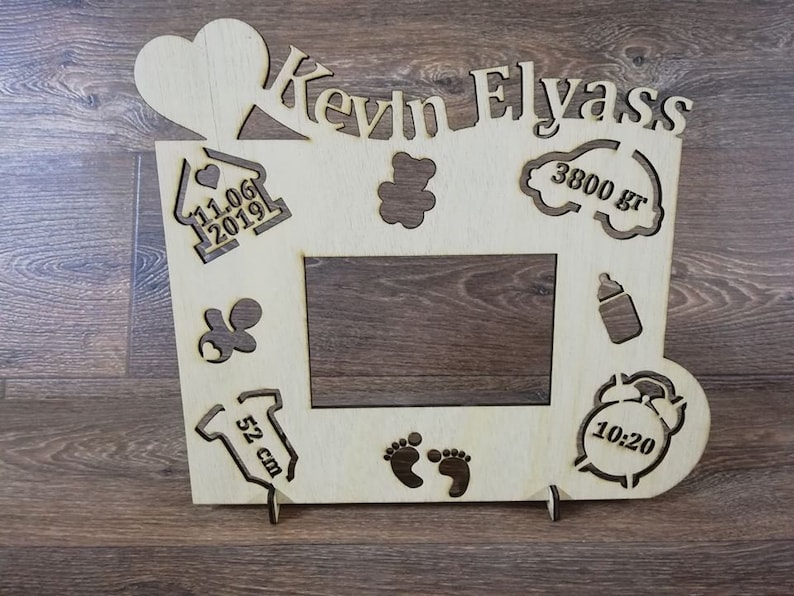 Pode incluir: Moldura de fotos de madeira com um cora&ccedil;&atilde;o, uma casa, um urso de peluche, uma nuvem, uma mamadeira, um macac&atilde;o, pegadas e um despertador. A moldura &eacute; personalizada com o nome "Kevin Elyass", a data "11.06.2019", o peso "3800 g", o comprimento "52 cm" e a hora "10:20".