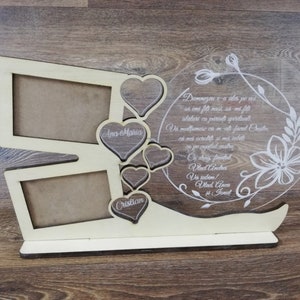 Könnte beinhalten: Ein Holzrahmen mit zwei rechteckigen Öffnungen und fünf herzförmigen Öffnungen. Die Herzen sind mit den Namen "Ana Maria" und "Cristian" graviert. Ein transparenter Acrylkrei mit einem Blumenmuster und einem gravierten Text ist am Rahmen befestigt. Der Text lautet: "Dumnezeu v-a ales pe voi sa imi fiti nasi, sa imi fiti alaturi ca parinti spirituali. Va multumesc ca m-ati facut Oaste, ca m-ati sprijinit si m-ati lasat sa joc capitolul asta minunat.  Ce drag finutati. Vlad Andrei.  Ves iubim! Vlad Anca si Janet."