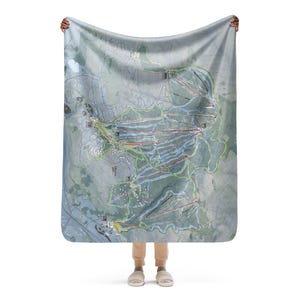 May include: A large, rectangular blanket featuring a detailed map of a ski resort. The map includes trails, lifts, and other features, rendered in shades of green, blue, and red against a gray background. The blanket is held up by a person.
