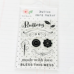 May include: Clear plastic packaging with a set of 8 clear stamps featuring a button theme. The stamps include the words "Buttons", "made with love", and "BLESS THIS MESS".