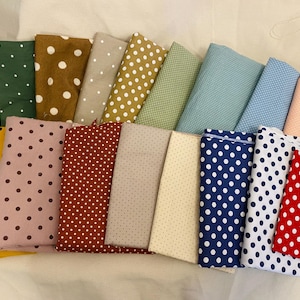 K&ouml;nnte beinhalten: Eine Sammlung gefalteter Stoffst&uuml;cke in verschiedenen Farben, jeweils mit einem Tupfenmuster versehen. Zu den Farben geh&ouml;ren Wei&szlig;, Gr&uuml;n, Braun, Beige, Gelb, Rosa, Rot, Blau und Pfirsich. Die Stoffe sind in einer ansprechenden Anordnung angeordnet.