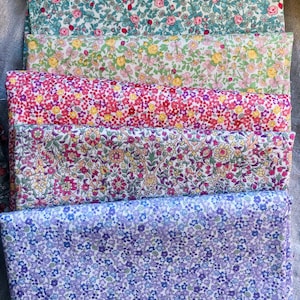K&ouml;nnte beinhalten: Ein Stapel bunter Stoffe mit Blumenmustern. Die Stoffe zeigen verschiedene Muster kleiner Blumen in Rosa-, Rot-, Gelb-, Gr&uuml;n- und Lilat&ouml;nen. Die Stoffe sind ordentlich gefaltet und &uuml;bereinander gestapelt, was die Vielfalt der Designs zeigt.