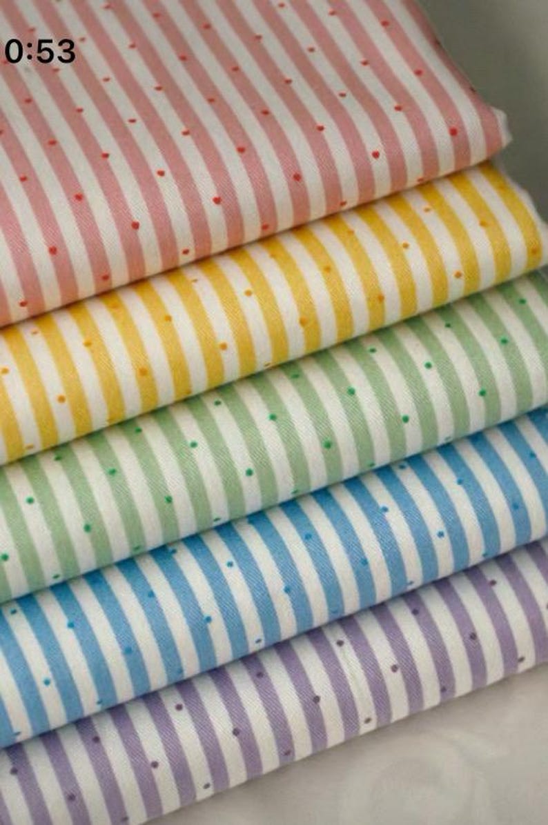 K&ouml;nnte beinhalten: Ein Stapel bunter Stoffmuster. Jeder Stoff hat vertikale Streifen in verschiedenen Farben: Rosa, Gelb, Gr&uuml;n, Blau und Lila. Kleine Punkte in einer Kontrastfarbe sind &uuml;ber die Streifen verteilt.