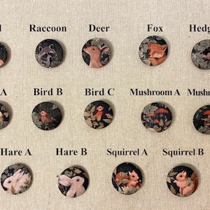 May include: A set of 12 round buttons featuring various woodland creatures and mushrooms. The buttons are black with a white background and feature detailed illustrations of an owl, raccoon, deer, fox, hedgehog, birds, mushrooms, hare, and squirrels.