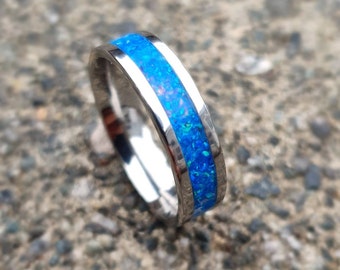 Pode incluir: Um anel de prata com uma incrustação de opala azul. A opala tem um acabamento brilhante e iridescente.