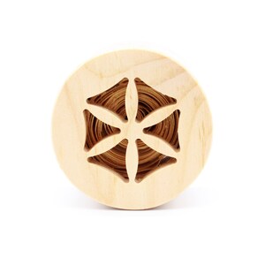 Può includere: Un rocchetto di legno con un motivo floreale tagliato. Il rocchetto è in legno chiaro e ha una finitura naturale.