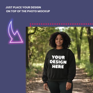 Puede incluir: Una sudadera negra con el texto "YOUR DESIGN HERE" en blanco. La sudadera la lleva puesta una persona con el pelo rizado en un entorno de bosque.