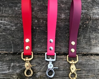 Könnte beinhalten: Drei Hundeleinen mit verschiedenen farbigen Riemen und goldenen Verschlüssen. Die Leinen sind rot, pink und burgunderrot.