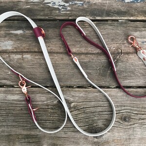 May include: Two leather dog leashes, one white and one burgundy, with rose gold hardware and clips.