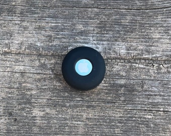 May include: A black round device with a white Apple logo on a wooden surface.