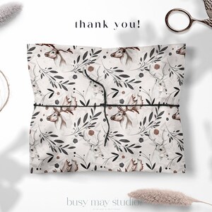 May include: A white gift bag with a brown and black deer and floral pattern. The bag is tied with a black string and the words "thank you!" are written in black above the bag.
