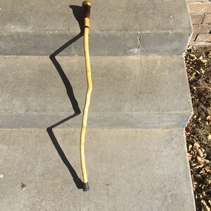 May include: A wooden walking stick with a brown and gold top and a black bottom. The stick is resting on a set of concrete steps.