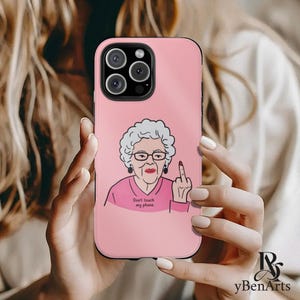 May include: Pink phone case with a cartoon illustration of an older woman with gray hair and glasses giving the middle finger. The text on the case reads "Don't touch my phone."