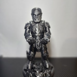 May include: A detailed, silver-colored figurine of a soldier in full armor, kneeling on a textured base. The figure has a stern expression and is holding a weapon. The armor has intricate details.