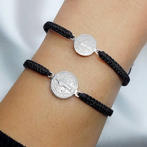 May include: Two black cord bracelets with silver medallions featuring a religious figure. The medallions are round and have a raised design.