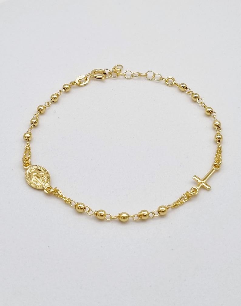 May include: A gold-toned rosary bracelet with a small oval charm and a cross charm.